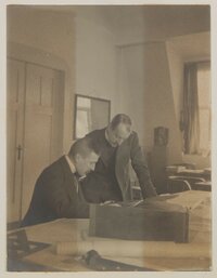 Hofmannsthal und van de Velde über einen Tisch mit Zeichnungen gebeugt